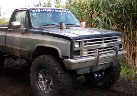 1978 Ford Bronco - This lifted pickup truck is parked off-road with tall grass in the background. It features prominent exhaust stacks and custom decals.