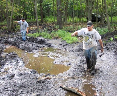 1978 Ford Bronco - Two men navigate a muddy, wooded area with a dark vehicle in the distance.