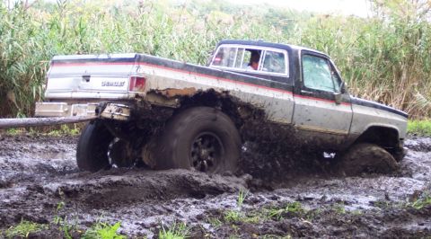 1978 Ford Bronco - A Chevrolet pickup truck is deeply stuck in mud, with its tires submerged and mud splashing around.