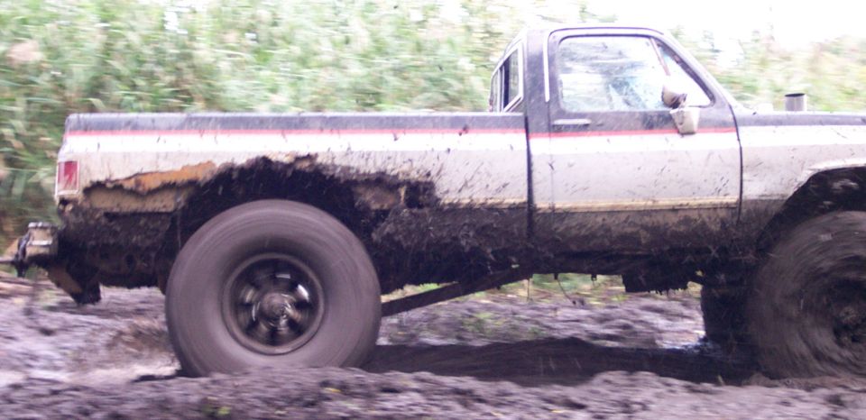 Side view of a muddy 1978 pickup truck driving through mud