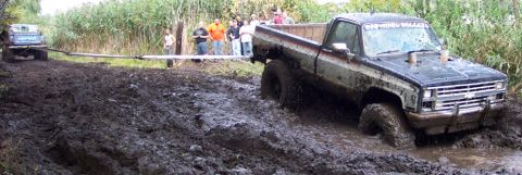 1978 Ford Bronco - Two trucks are stuck in thick mud while onlookers observe the off-road challenge.