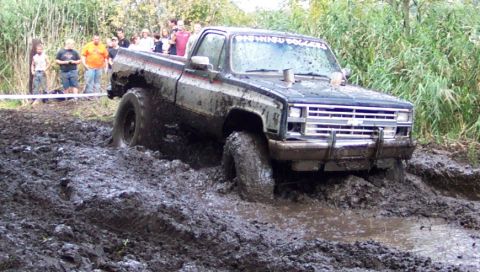 1978 Ford Bronco - A heavily muddied pickup truck navigates a challenging off-road course, with onlookers in the background.