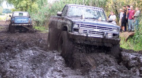 1978 Ford Bronco - Two pickup trucks are stuck in thick mud during an off-road event.