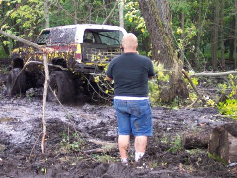 1978 Ford Bronco - A 1978 Ford Bronco is deeply stuck in mud and debris in a wooded area, with a person standing nearby.