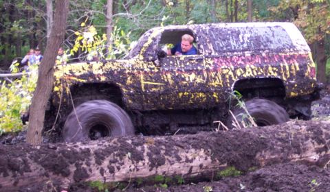 1978 Ford Bronco - SUV stuck deep in mud and logs, with a driver visible.