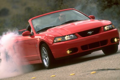 2003 Ford Mustang - A red 2003 Ford Mustang convertible is shown performing a burnout, with smoke billowing from the rear tire.