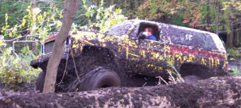 1978 Ford Bronco - A heavily mud-splattered SUV is stuck in a muddy ditch, with a driver visible inside.