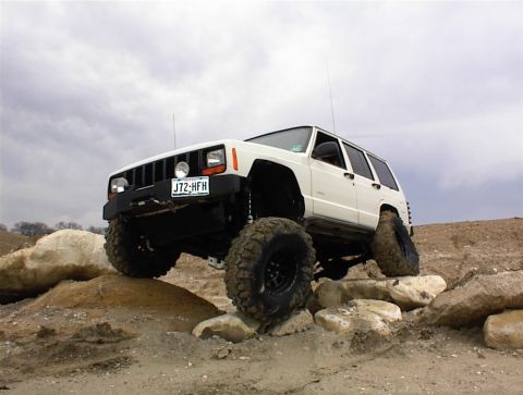 1986 Ford Bronco - A white Jeep Cherokee XJ navigates a rocky off-road course, demonstrating its climbing capabilities.