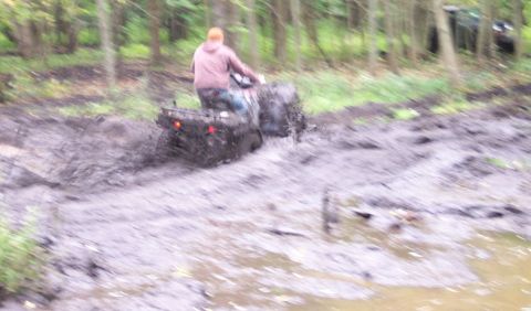 1978 Ford Bronco - An ATV navigates through a challenging muddy terrain in a wooded environment.