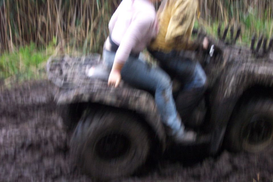 Mud-covered ATV with two people riding through a muddy field with tall grass
