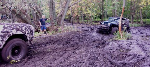 1978 Ford Bronco - Two off-road vehicles are stuck in a muddy wooded area, one being pulled by a rope.