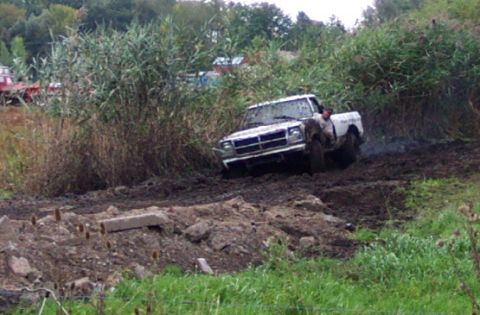 1978 Ford Bronco - A white pickup truck navigates a muddy off-road course, with dense vegetation surrounding the track.