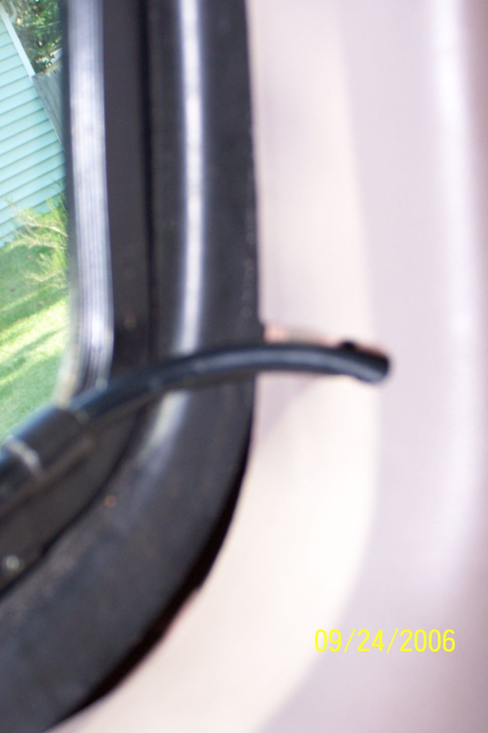 Close-up of a black cable end near a window frame inside a vehicle, beige interior panel behind, dated 09/24/2006.