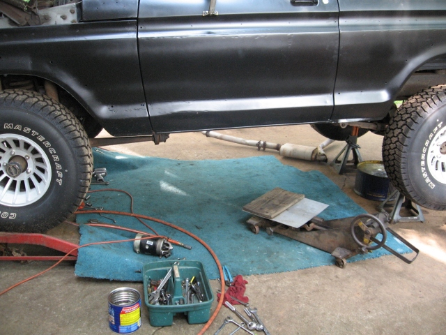 Black Ford truck on jack stands over a garage floor with transmission jack and tools laid out