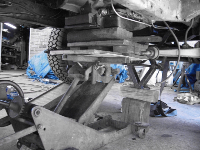 Truck axle and leaf spring supported on a floor jack with wood blocks in a garage
