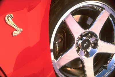 2003 Ford Mustang - Close-up of a red car's fender with a Cobra emblem and a chrome SVT wheel with Cobra brake calipers.