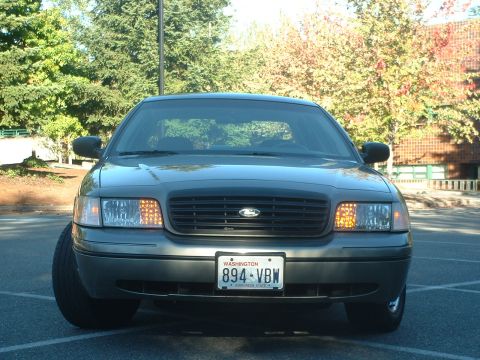 2000 Ford Crown Victoria - A 2000 Ford Crown Victoria is shown from the front, parked in a lot with trees and a building in the background.