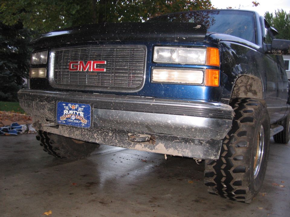 Black lifted GMC truck front end with muddy off-road tires in a driveway