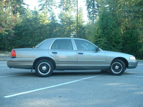 2000 Ford Crown Victoria - A silver 2000 Ford Crown Victoria is parked in an outdoor lot with trees in the background.