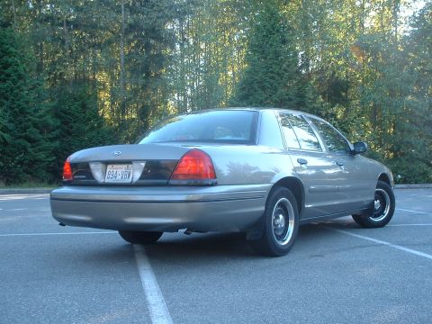 2000 Ford Crown Victoria - Rear view of a silver 2000 Ford Crown Victoria parked in a lot with trees in the background.