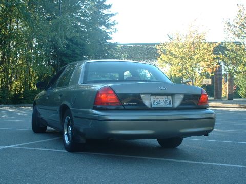 2000 Ford Crown Victoria - The rear of a Ford Crown Victoria is shown parked in an outdoor lot with trees and a basketball hoop in the background.