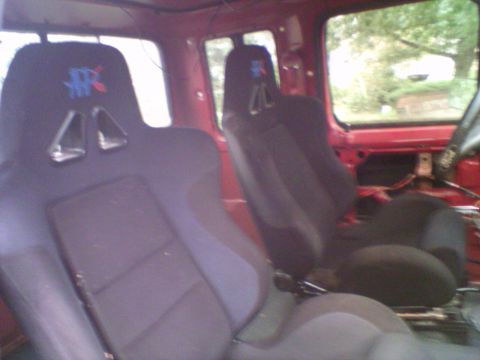 1985 Ford F-150 - Aftermarket racing seats are installed in the interior of a red vehicle, with a view out the window.