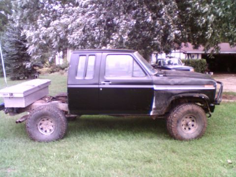1985 Ford F-150 - A black extended cab pickup truck sits on a grassy lawn with trees in the background.