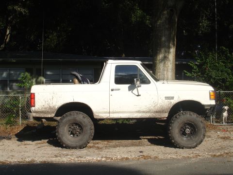 1989 Ford Bronco - This lifted 1989 Ford Bronco is shown from the side, large off-road tires and a white exterior.