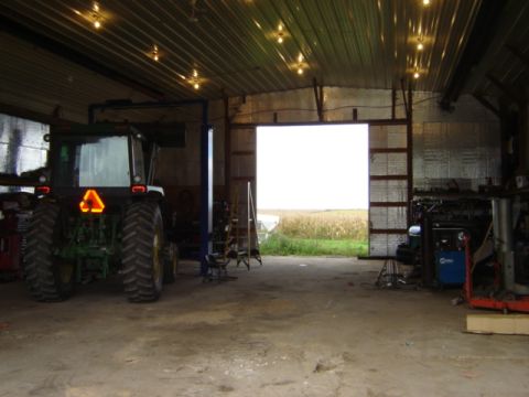 1992 Ford Bronco - A tractor is parked inside a garage, with a large open doorway revealing a field of crops.