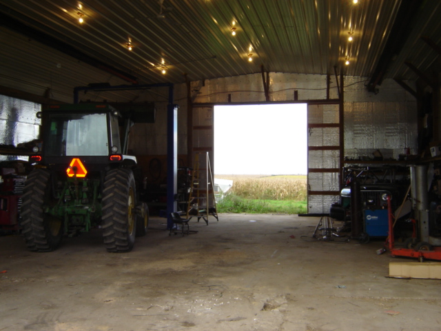 Tractor rear view inside a garage with an open bay door showing a field