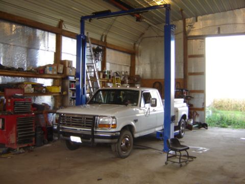 1992 Ford Bronco - A white pickup truck is positioned on a two-post vehicle lift inside a workshop.