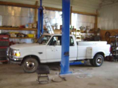 1992 Ford Bronco - A white 1992 Ford Bronco pickup truck is positioned on a hydraulic lift inside a workshop.