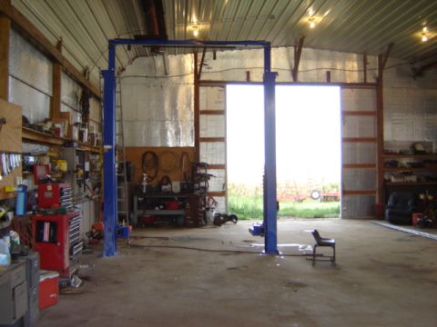 1992 Ford Bronco - Interior view of a workshop a car lift, tool chests, and shelving, with an open bay door revealing an outdoor scene.