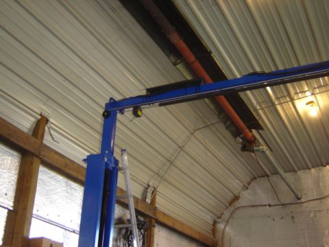 1992 Ford Bronco - The interior of a workshop features a blue car lift and a corrugated metal ceiling with exposed pipes and wiring.