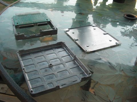 1991 Ford Bronco - An electronic control unit is shown disassembled, revealing its internal circuit board and protective metal casing components.