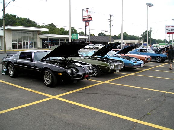 Black 1977 Pontiac Firebird with hood open, parked in a lot with other classic cars