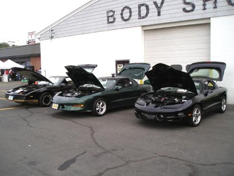 1994 Pontiac Trans Am - Several Pontiac Firebirds are parked outside a building with 'BODY SHOP' visible on the facade.