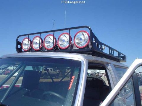 1996 Ford Bronco - This silver SUV, identified as a 1996 Ford Bronco, features a roof rack equipped with five large spotlights.