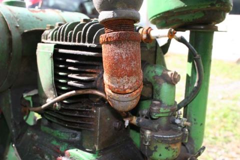 1987 Ford Bronco - Close-up view of a green engine with visible rust on its exhaust pipe and spark plug.