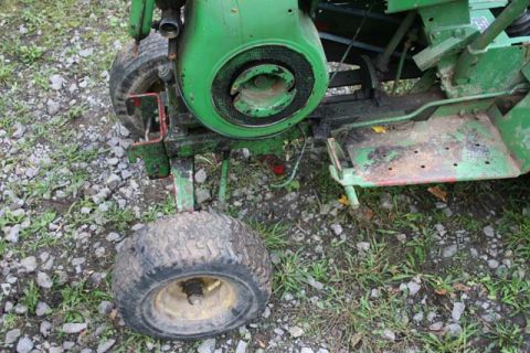 1987 Ford Bronco - Close-up view of a green riding mower's engine and front wheel, resting on gravel and grass.