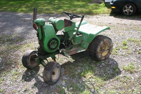 1987 Ford Bronco - A green riding mower sits on a gravel driveway next to a dark car.