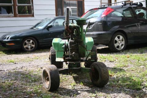 1987 Ford Bronco - A green riding mower sits in front of two cars parked on a gravel driveway.