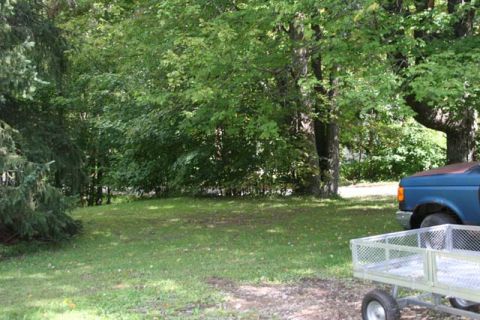 1987 Ford Bronco - A blue truck with a brown hood is partially visible on the right side of the frame, parked on a lawn.