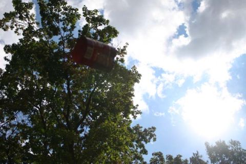 1987 Ford Bronco - A red can is captured mid-air against a backdrop of trees and a bright, cloudy sky.