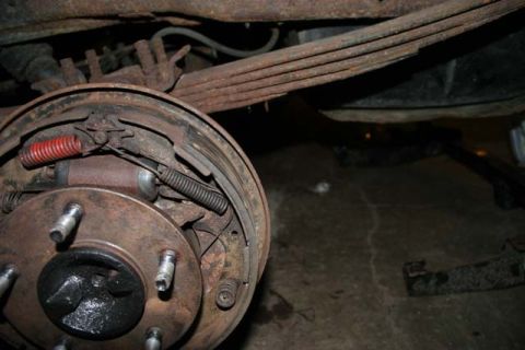 1987 Ford Bronco - Close-up view of a rusty rear drum brake assembly and leaf springs.