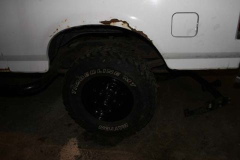 1987 Ford Bronco - The rear wheel well of a white vehicle shows significant rust around the fender opening.