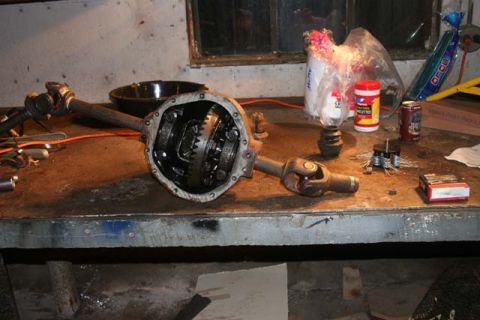 1987 Ford Bronco - A disassembled differential and driveshaft lie on a cluttered workbench.