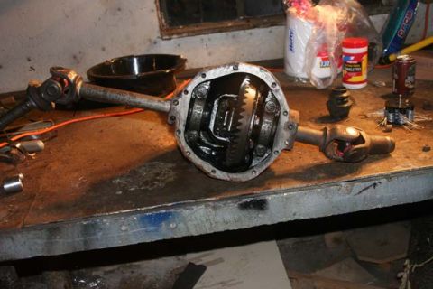 1987 Ford Bronco - Differential and driveshaft assembly resting on a workbench with tools and supplies in the background.