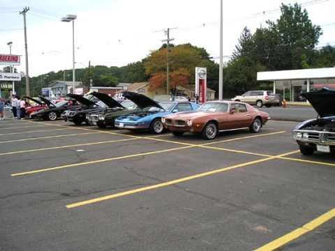 1994 Pontiac Trans Am - A line of classic Pontiac Firebirds are parked in a lot with their hoods open, suggesting a car show or meet-up.