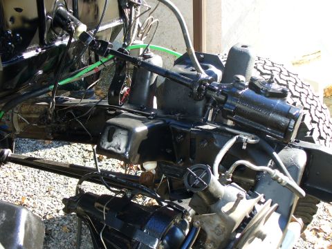 1978 Ford Bronco - Overhead view into a stripped truck front end showing a black-painted steering box bolted to the frame rail, the steering shaft and rag joi…